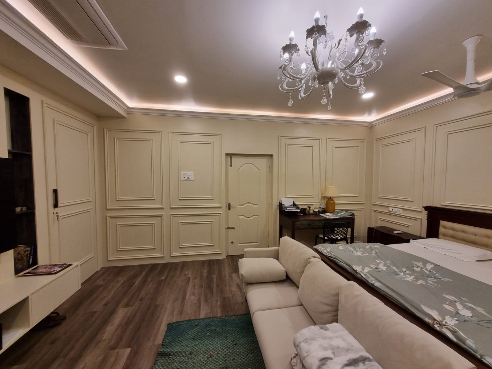 Completed master bedroom with paneled walls, chandelier, warm flooring, and coordinated furniture